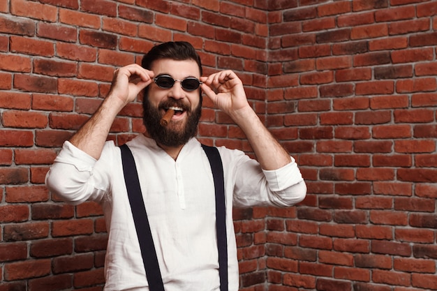 Young handsome man laughing holding cigar on brick wall.