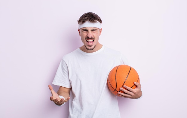 怒って、イライラして欲求不満に見える若いハンサムな男。バスケットボールの概念
