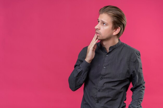 Young handsome man looking aside with pensive expression on face standing over pink wall