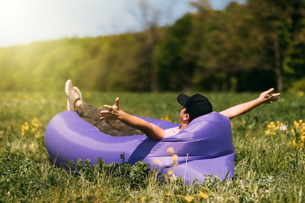 Free photo young handsome man lying on the air sofa lamzac, near the forest