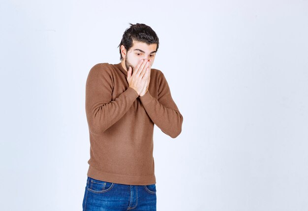 A young handsome man model in brown sweater covering his mouth . High quality photo