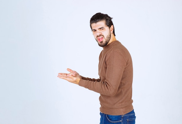 модель молодого красивого человека стоя в коричневом свитере и позируя над белой стеной.