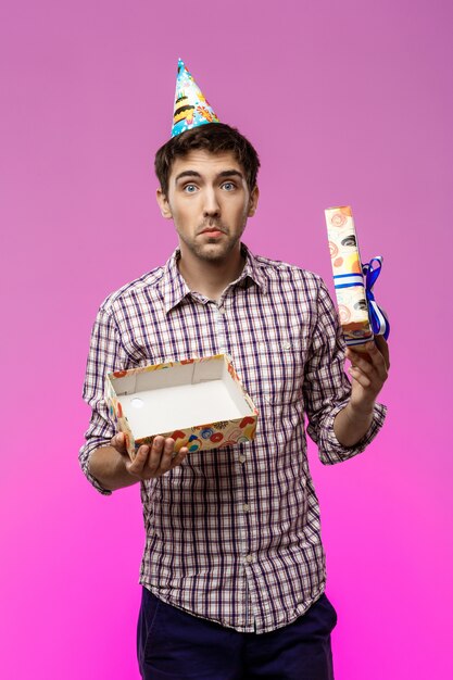 Young handsome man opening birthday gift over purple wall.