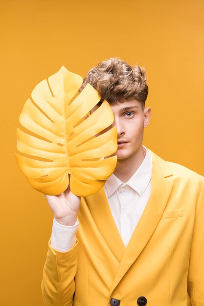 Young handsome man behind palm leaf in a yellow scene