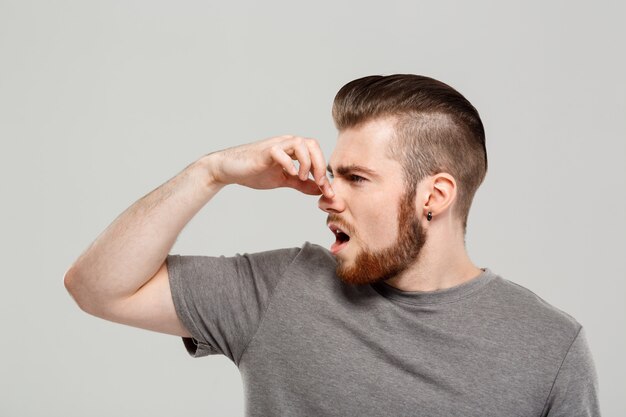 Young handsome man pinching nose over grey wall.