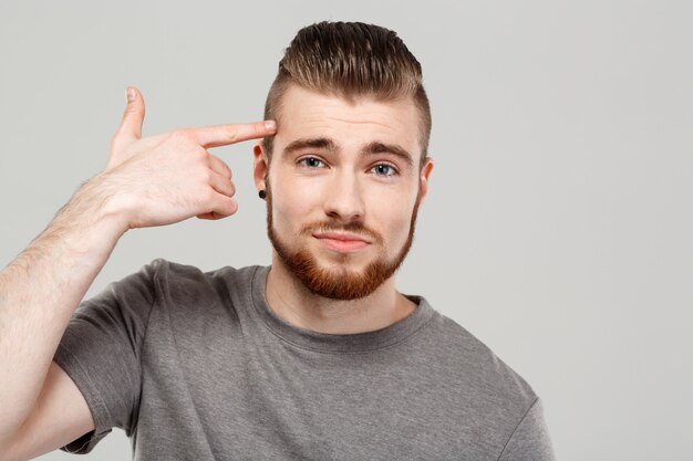 Young handsome man pointing finger in head over grey wall.