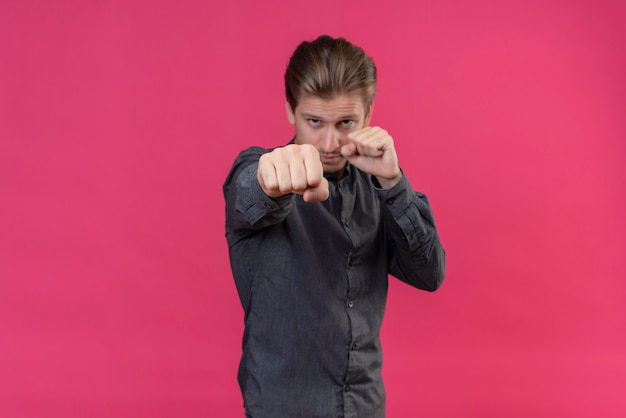 Free photo young handsome man posing like boxer with clenched fists standing over pink wall