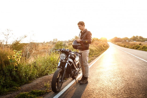 田舎道で彼のバイクに近いポーズの若いハンサムな男。