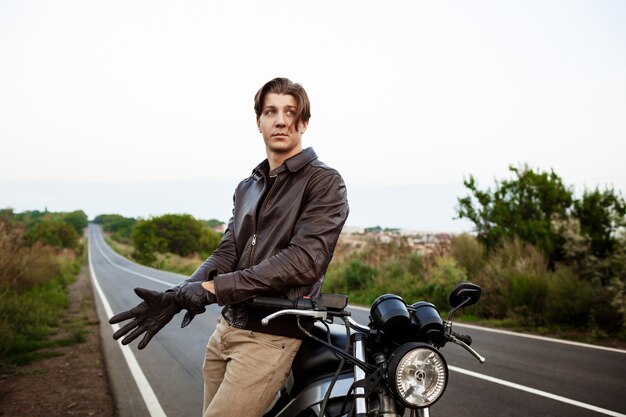 Young handsome man posing near his motorbike, wearing gloves.