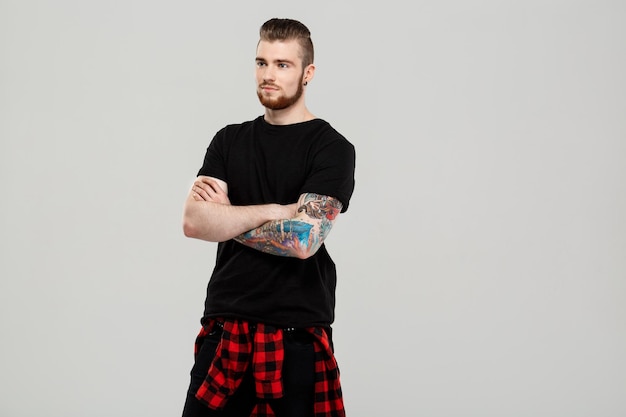 Young handsome man posing, smiling, looking at front, arms crossed over grey wall