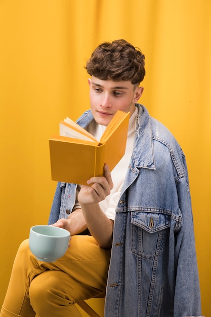 Free photo young handsome man reading a book in a yellow scene