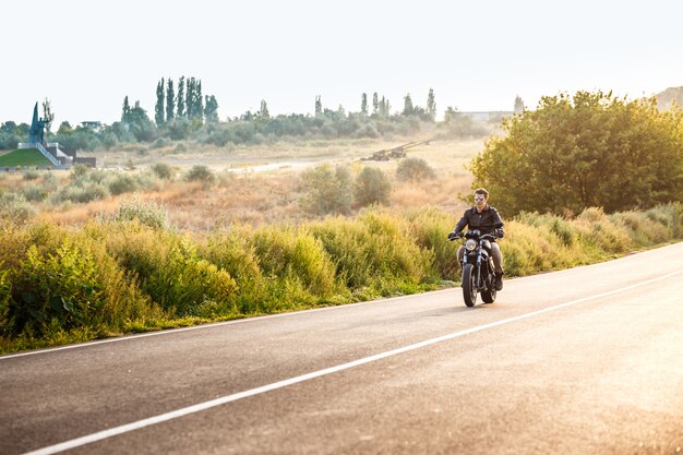 Young handsome man riding on motorbike at countryside road.