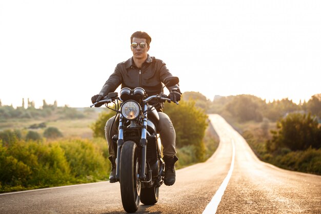 田舎道でバイクに乗って若いハンサムな男。