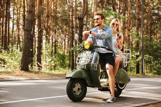 Foto gratuita giovane uomo bello sul motorino con la macchina fotografica della tenuta dell'amica