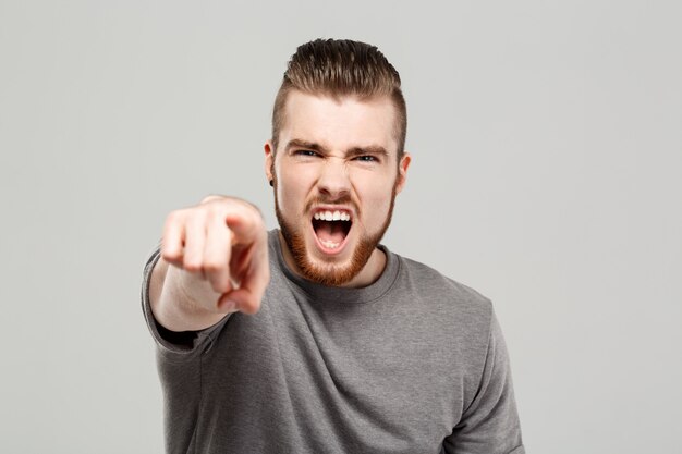 Young handsome man shouting over grey wall.