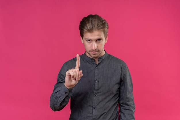 Free photo young handsome man showing index finger asking to wait with confident expression standing over pink wall