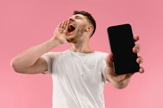 Young handsome man showing smartphone screen isolated on pink background in shock with a surprise