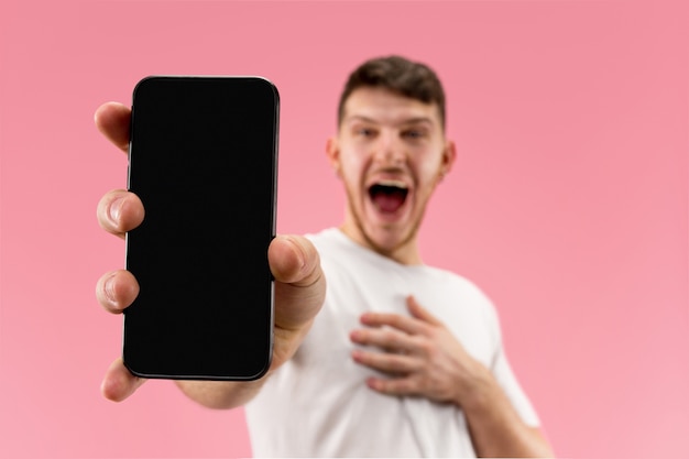 Young handsome man showing smartphone screen over pink space with a surprise face