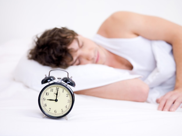 Free photo the young handsome man sleeping with alarm clock near his head