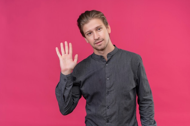 Young handsome man smiling friendly waving with hand standing over pink wall