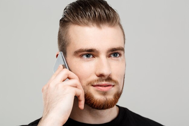 Young handsome man speaking on phone over grey wall.