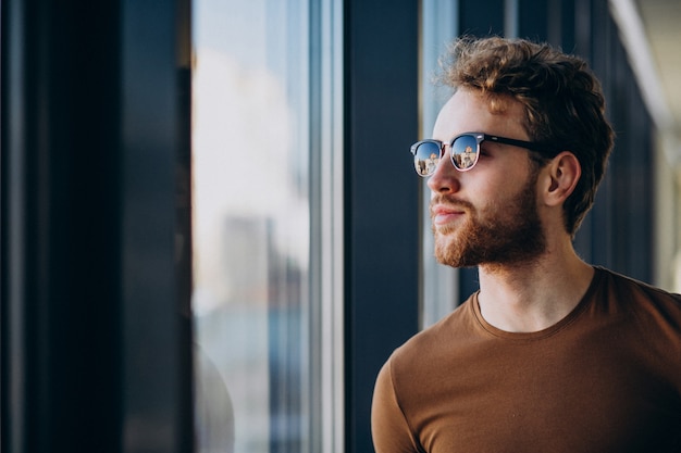 Free photo young handsome man standing by the window at the airport