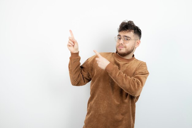 young handsome man standing and pointing over white wall. 
