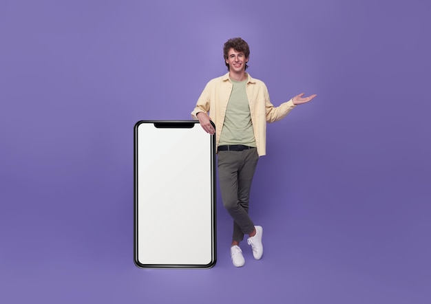 Free photo young handsome man standing with mockup big smartphone blank white screen on purple background