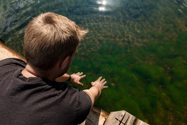 Free photo young handsome man stretching hands in lake with fish