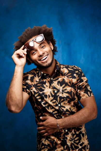 Young handsome man in sunglasses posing over blue surface