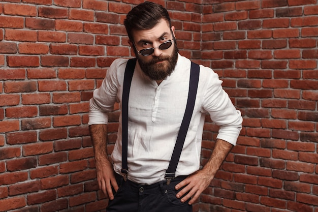 Young handsome man in sunglasses posing on brick wall.