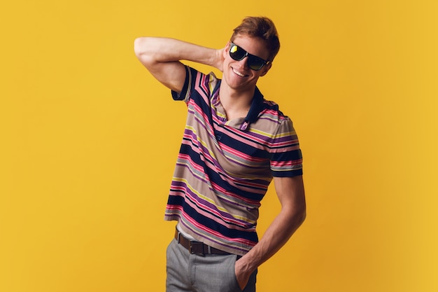 Young handsome man in sunglasses wearing casual t-shirt standing over yellow wall looking with smile on face, natural expression. laughing confident