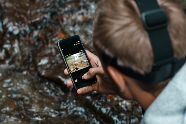 Young handsome man taking close up photo of waterfall