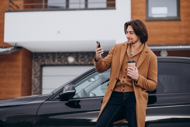 Young handsome man talking on the phone by his car