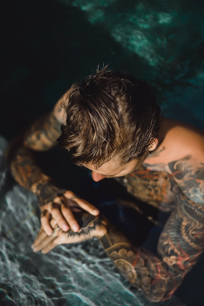 Foto gratuita giovane uomo bello in tatuaggi che riposa nella piscina all'aperto.