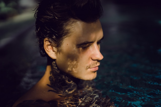 молодой красивый человек в татуировки отдыхает в открытом бассейне.