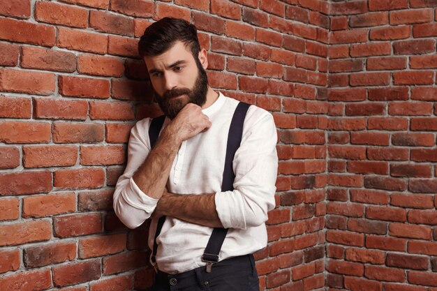 Young handsome man thinking posing on brick wall.