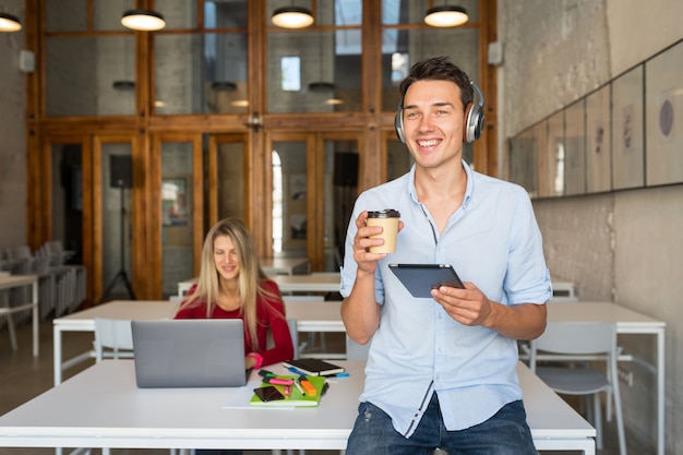 Young handsome man using tablet listening to music on wireless headphones,