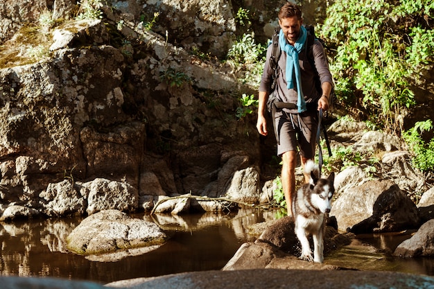 Young handsome man walking with huskies dog in canyon near water