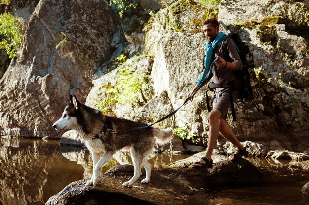 Молодой красивый человек гуляя с собакой хаски в каньоне около воды