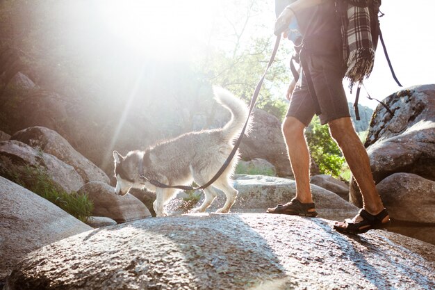 Молодой красивый человек гуляя с собакой хаски в каньоне около воды
