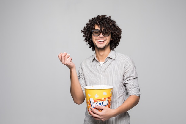 Молодой красавец носить 3d очки с вьющимися волосами, держа миску попкорна над изолированной белой стеной