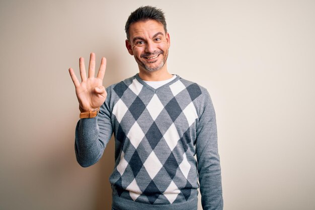 Young handsome man wearing casual sweater standing over isolated white background showing and pointing up with fingers number four while smiling confident and happy
