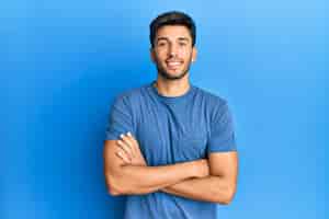 Free photo young handsome man wearing casual tshirt over blue background happy face smiling with crossed arms looking at the camera. positive person.