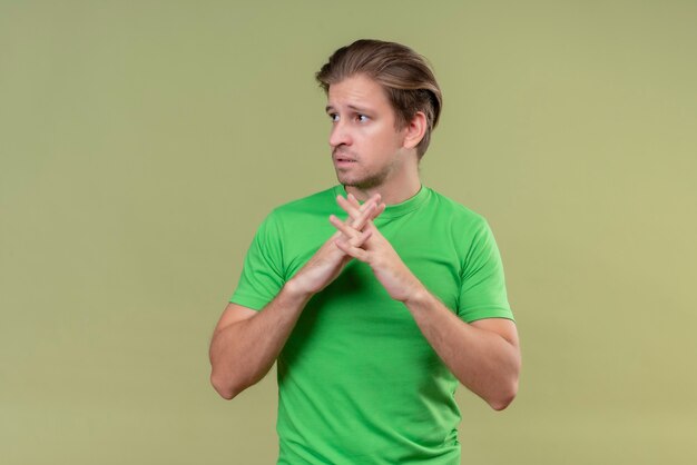 緑の壁を越えて立っている顔に悲しそうな表情でよそ見一緒に手を繋いでいる緑のtシャツを着ている若いハンサムな男
