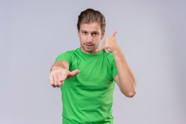 Young handsome man wearing green t-shirt pointing to the front and making call gesture