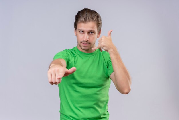 緑のtシャツを着て前面を指していると呼び出しジェスチャーを作る若いハンサムな男