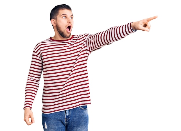 Free photo young handsome man wearing striped sweater pointing with finger surprised ahead, open mouth amazed expression, something on the front