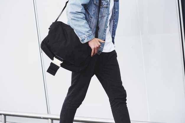 空港に急いで彼の肩にバッグを持つ若いハンサムな男。