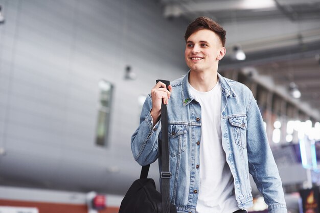 Young handsome man with a bag on his shoulder in a hurry to the airport.